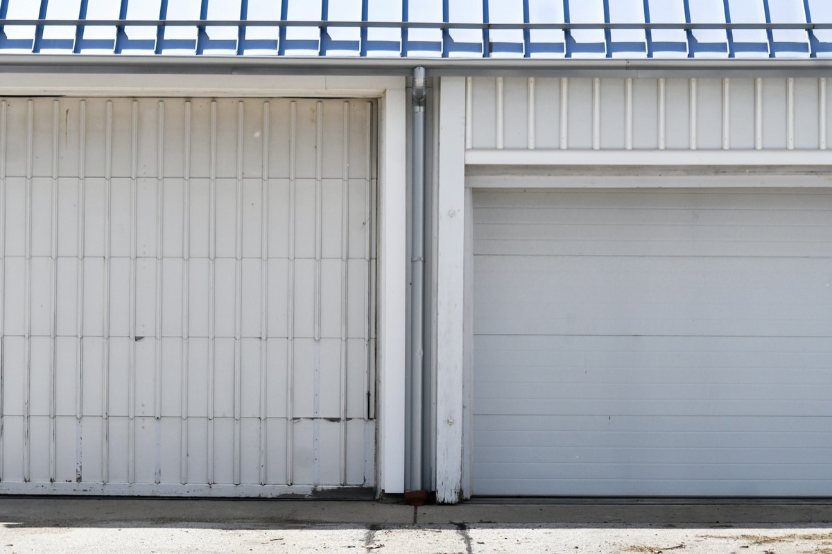 Two white residential garage doors under a blue metal roof
