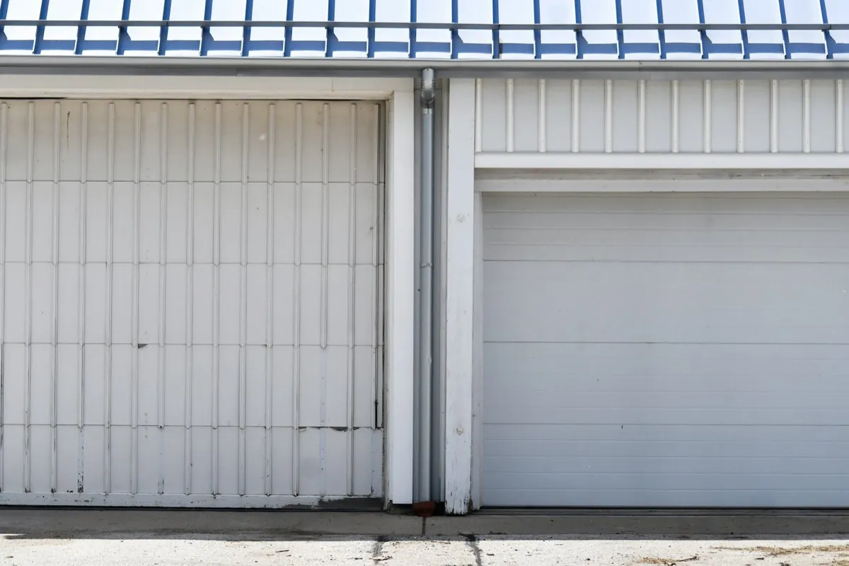 Two white residential garage doors under a blue metal roof