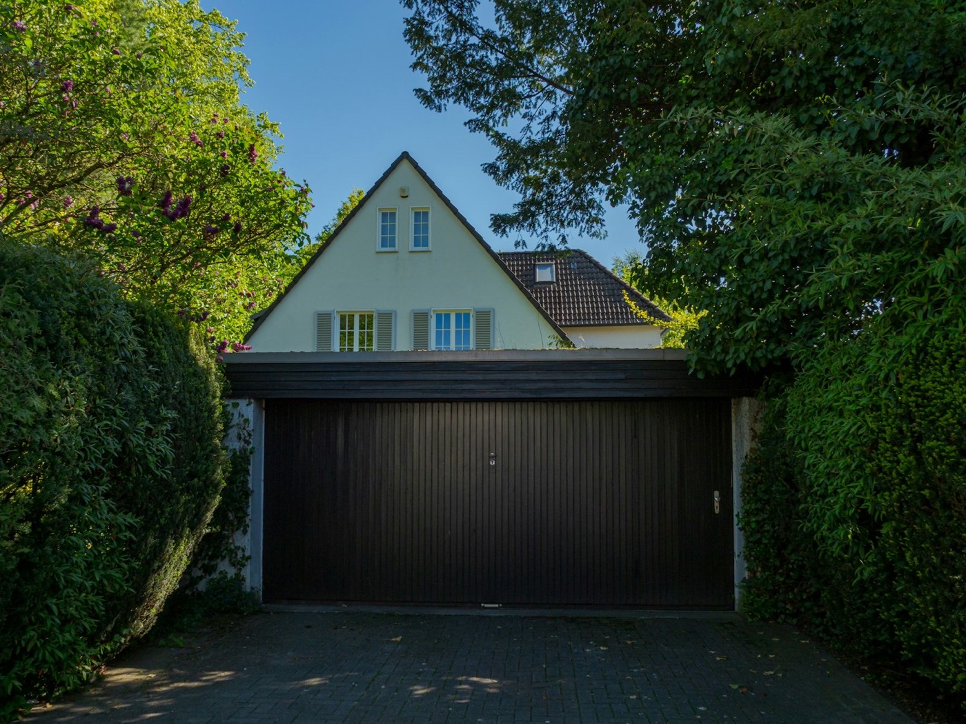 Dark double residential garage door framed by hedges at a family home